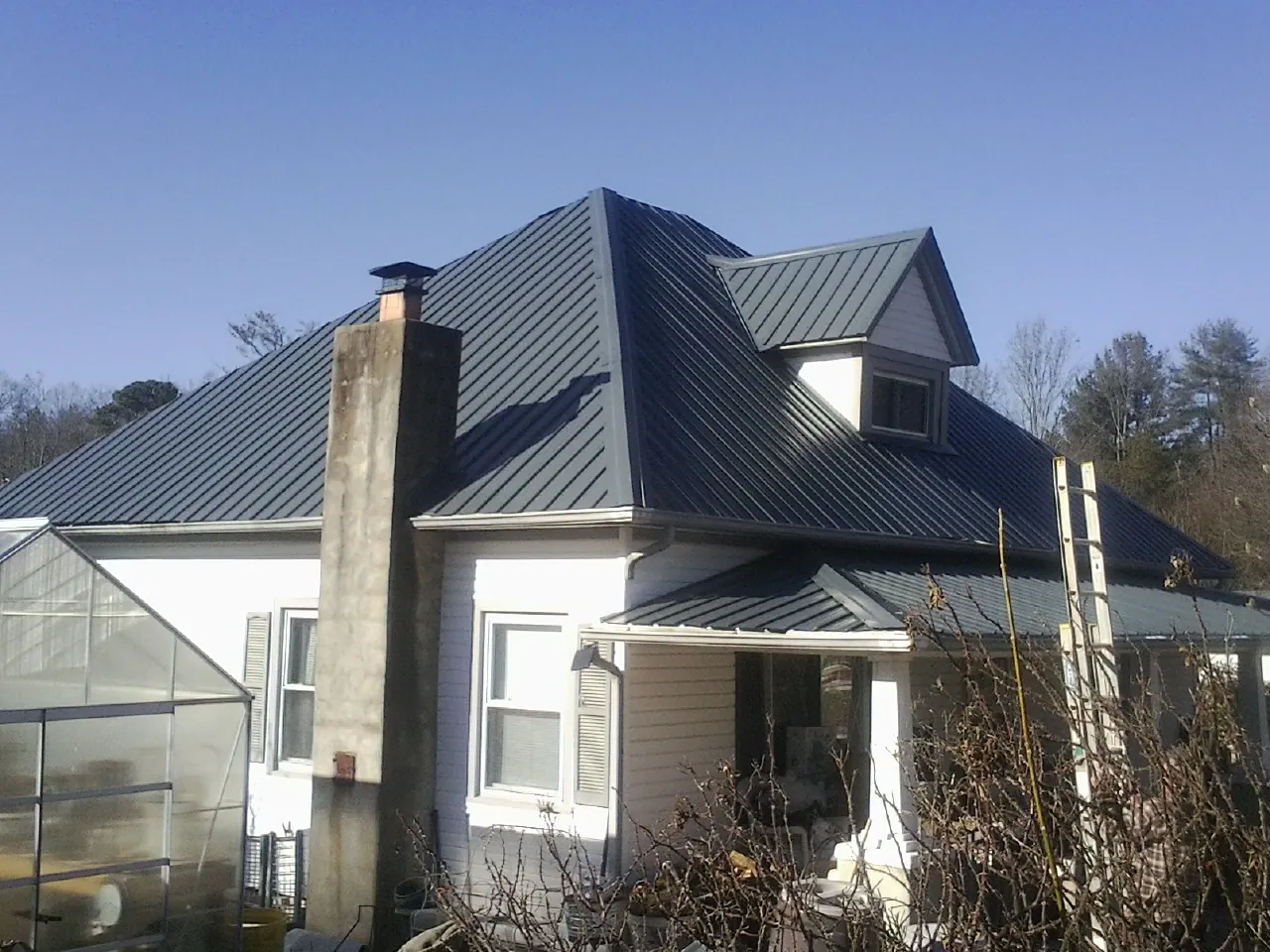 Dark blue standing seam metal roof on a white farmhouse with dormer — Slate & Tile Roof Repair by Roofing Brothers in Fallsburg