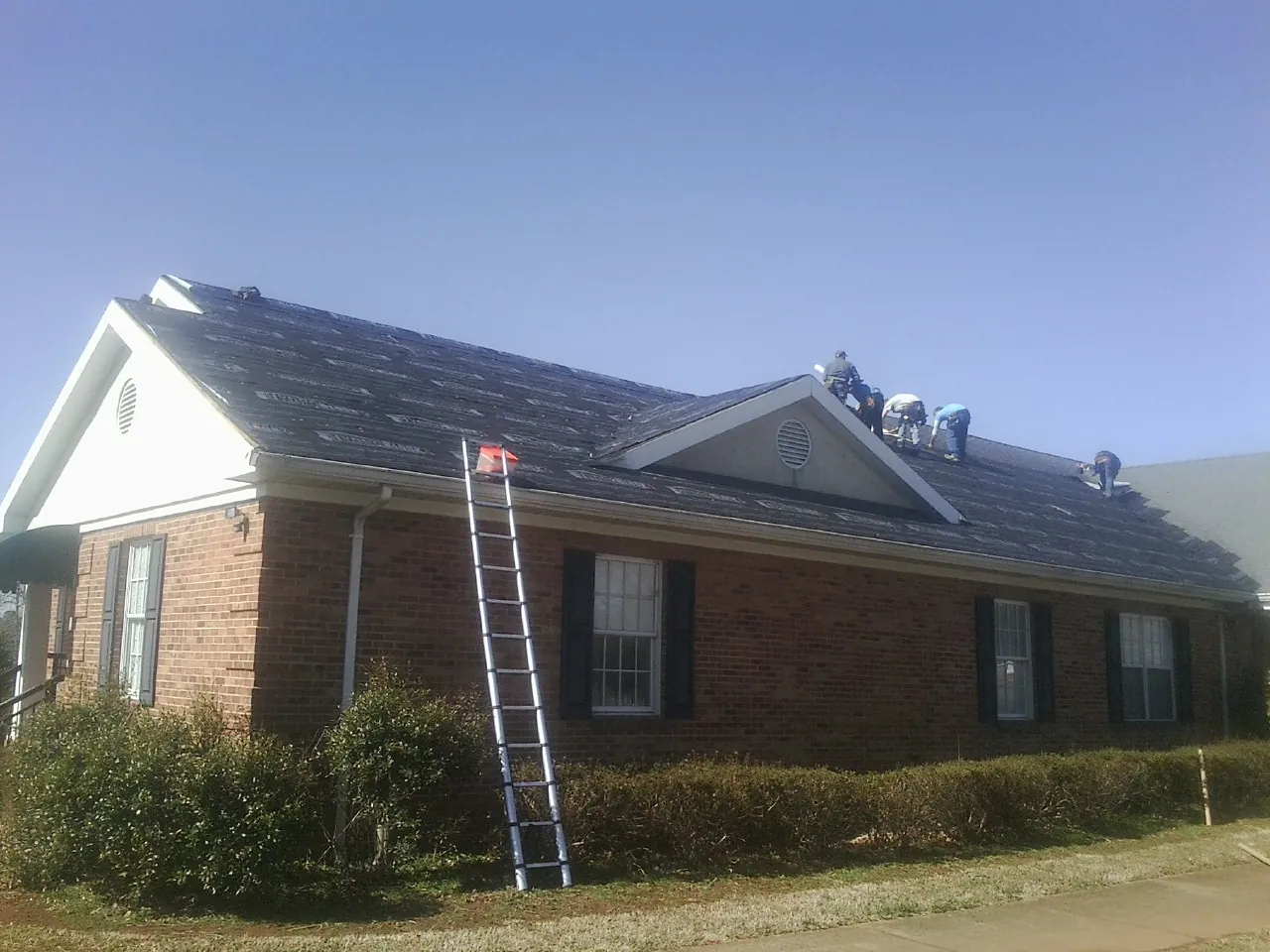 Crew tearing shingles off a brick ranch roof with a ladder set — Emergency Roof Repair work by our crew in Fallsburg
