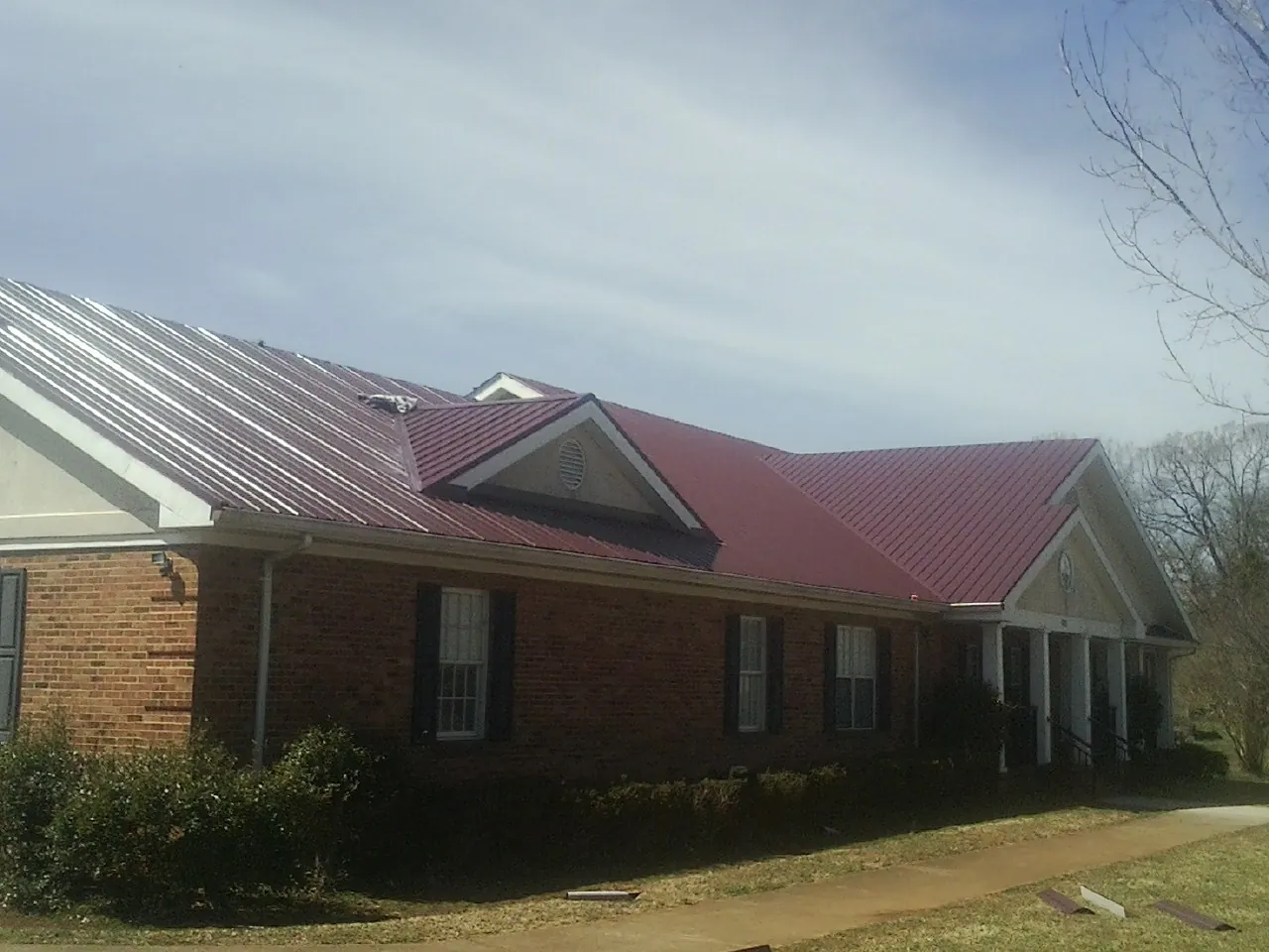 Red metal roof with gabled entries on a long brick building, from a Hail Damage Roof Repair job in Fallsburg
