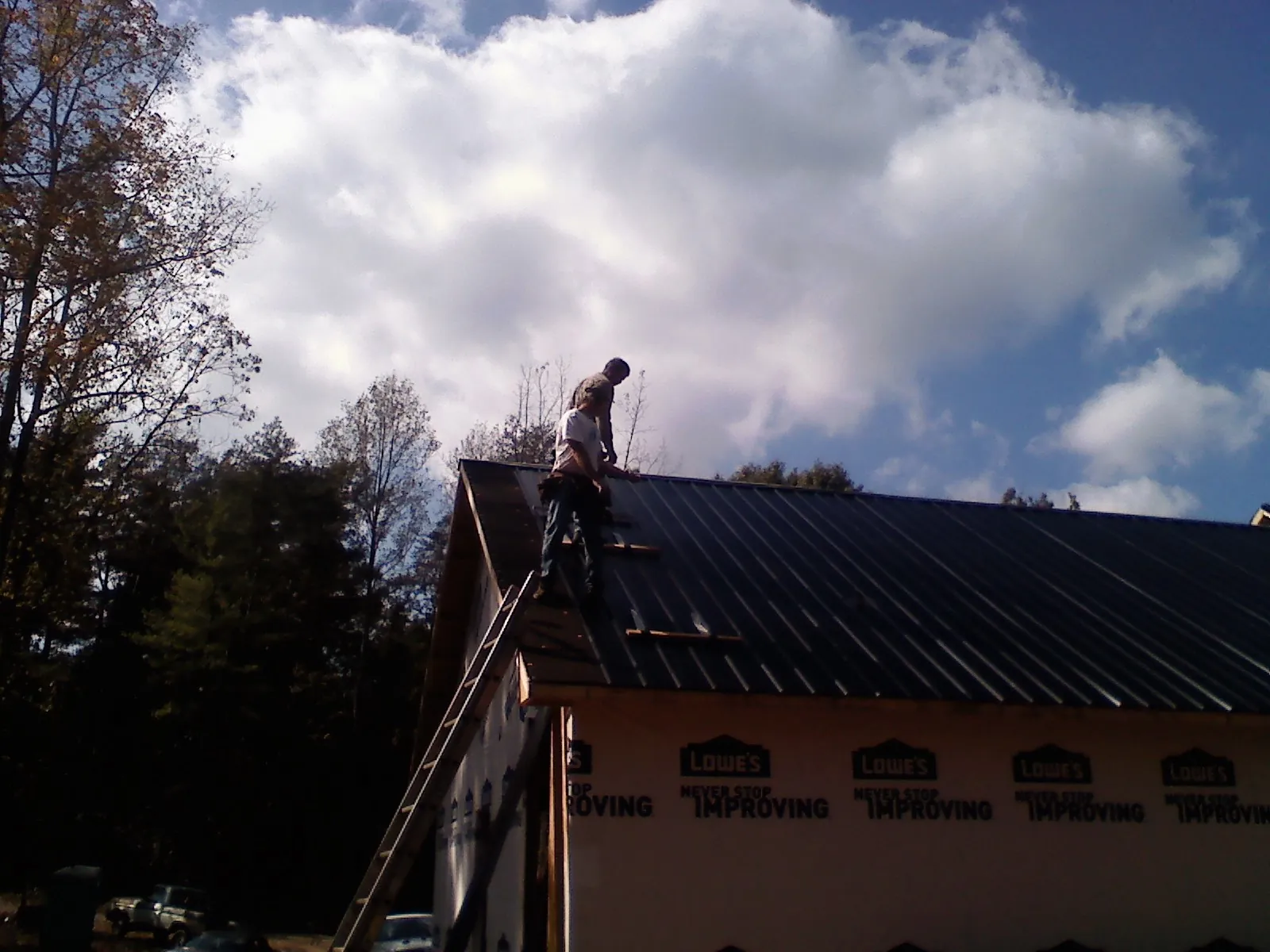 Roofer fastening dark metal panels high against a cloudy sky, from a Roof Inspection job in Fallsburg