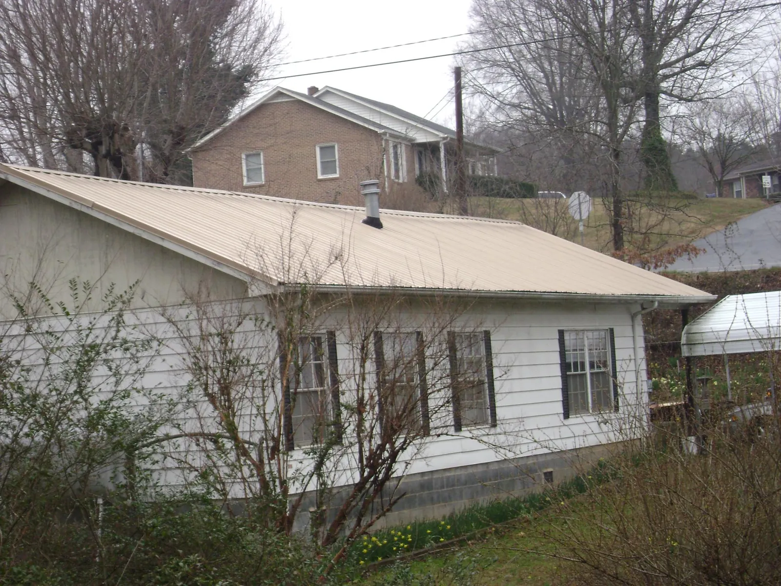 Tan metal roof on a white sided house set into a hillside — Commercial Roofing by Roofing Brothers in Fallsburg